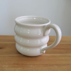 a stack of white cups sitting on top of a wooden table next to a wall