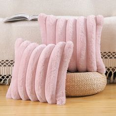 a pile of pink pillows sitting on top of a wooden floor next to a basket