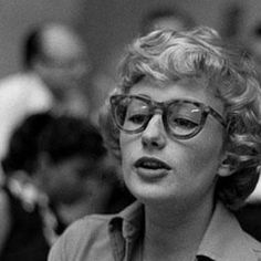 black and white photograph of a woman with glasses talking to someone in front of her