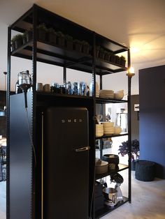 a black refrigerator sitting inside of a kitchen next to a shelf filled with pots and pans