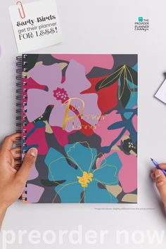 a person's hand is holding a pen and writing on a notebook with flowers