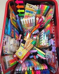 a red shopping cart filled with lots of different types of pens and markers on top of each other