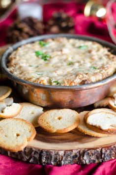 a bowl of dip surrounded by crackers on a wooden board with red cloth and other food items