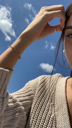 a woman is holding her hair up to her head and looking at the camera with a blue sky in the background