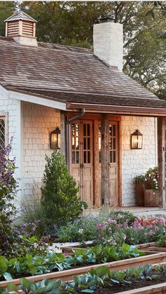 a small white house with lots of plants and flowers