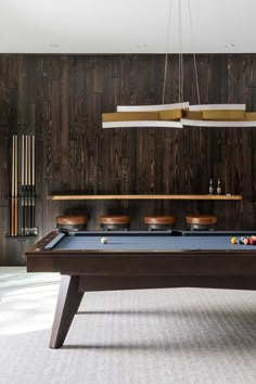 a pool table in a room with wood paneling on the walls and ceiling lights hanging above it