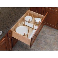 an open drawer in the middle of a kitchen counter with plates and cups on it