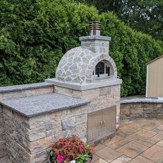 an outdoor pizza oven built into the side of a stone wall with potted plants