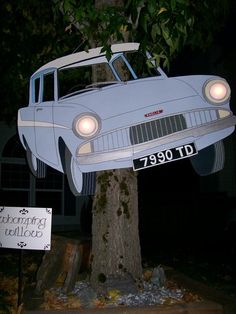 an old car is suspended from a tree in front of a sign that says,