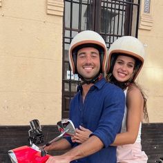 a man and woman on a scooter in front of a building smiling at the camera