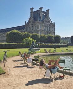 people lounging on lawn chairs in front of a large building with a pond and fountain