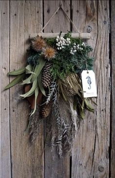 a wreath hanging on the side of a wooden wall with pine cones and other plants