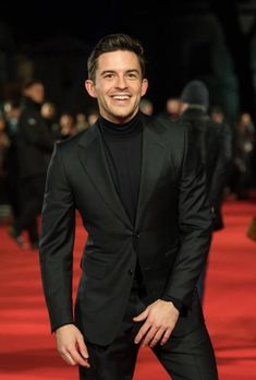 a man in a black suit standing on a red carpet with his hands in his pockets