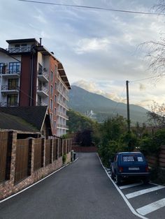 a car parked on the side of a road next to a tall building with mountains in the background