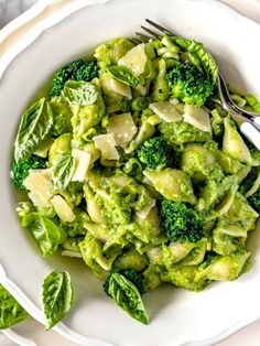 a white bowl filled with pasta and broccoli on top of a table next to silverware