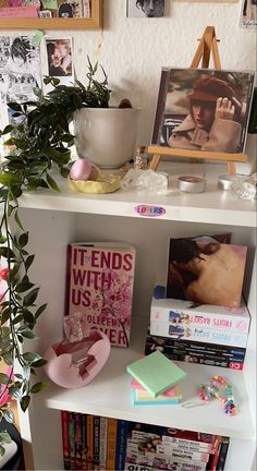 a book shelf filled with books next to a potted plant and pictures on the wall