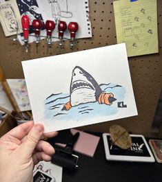 a person holding up a card with a drawing of a shark in the middle of it