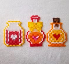 three small cross stitch purses with hearts and perfume bottles in them on a white surface