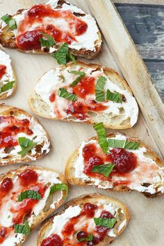 several pieces of bread with cheese and sauce on them sitting on a wooden tray next to some minty garnish