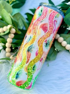 a colorful tumbler sitting on top of a white blanket next to some green leaves