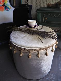 a white ottoman with tassels and a cup on it