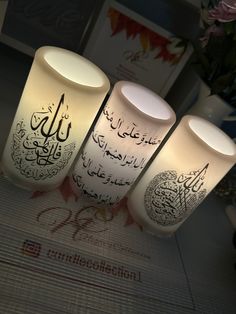 three lit candles with arabic writing on them