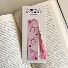 a bookmark with pink bows and hearts on it sitting next to an open book