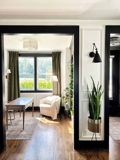 a living room filled with furniture and a large window next to a wooden floor covered in plants