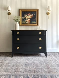 a black dresser with two vases sitting on top of it next to a painting