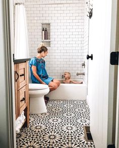 a woman and child sitting in a bathtub with black and white tiles on the floor