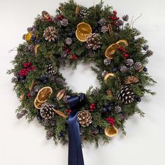 a christmas wreath with pine cones, oranges and other holiday decorations hanging on a wall