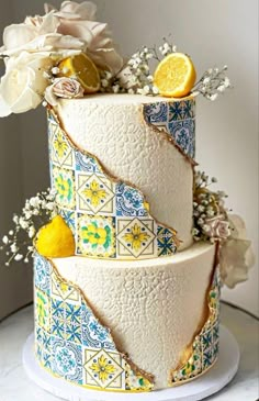 a three tiered cake with lemons and flowers on the top is decorated in blue, yellow and white