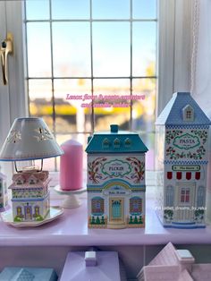 some little houses are on a table with a lamp in front of the window,