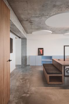 an office with concrete walls and flooring has a bench in the foreground as well as a wooden door on one side