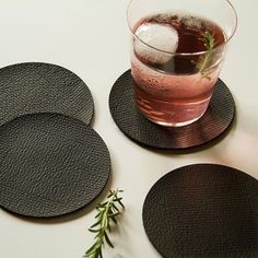 three black coasters and a drink on a white table top with rosemary sprig