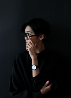 a woman in black shirt and glasses holding her hand to her face