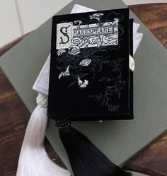 a black book sitting on top of a wooden table next to a white tassel