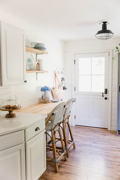 a kitchen with white cabinets and wood floors, along with an island counter that has stools in front of it