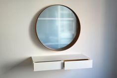 a round mirror on the wall above a white shelf