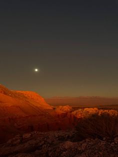 the moon shines brightly in the sky above some rocky hills and desert terrain at night