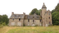 an old stone building in the middle of a field with tall grass and trees around it