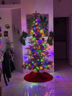 a brightly lit christmas tree in the corner of a room with white tile flooring