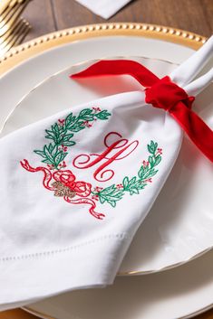 a white plate topped with a napkin covered in red ribbon and an embroidered monogram