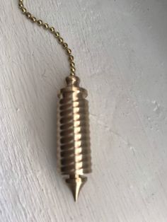 a metal object hanging from a chain on a white wall with a gold ball chain attached to it