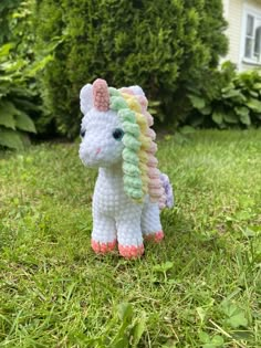 a small crocheted unicorn sitting on top of a green grass covered field in front of a house