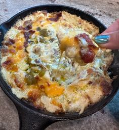 a person is dipping something into a skillet with cheese and other toppings on it