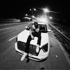 a man sitting on the hood of a car in the middle of an empty road