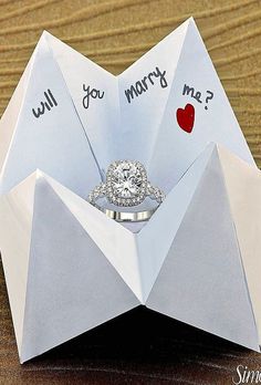 an origami envelope with two engagement rings in it and will you marry me? written on the inside