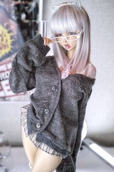 a doll wearing glasses and a sweater with cat ears on her head is posing for the camera