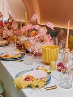 the table is set with pink and yellow flowers, candles, and place settings for dinner